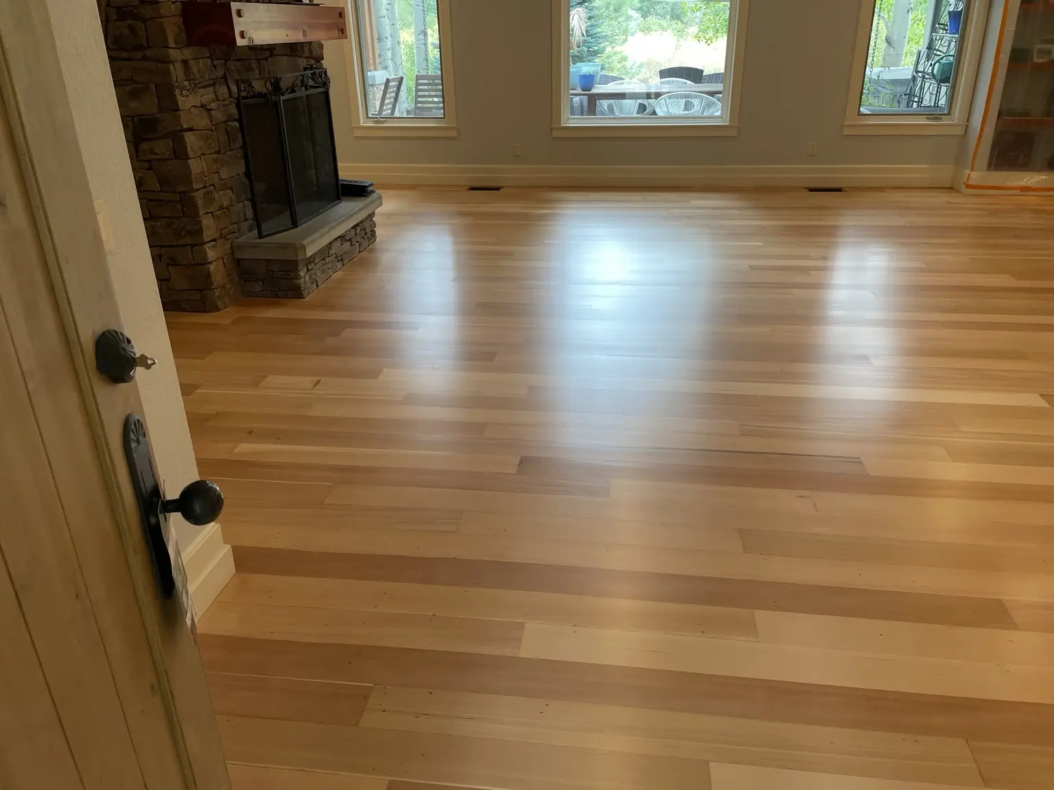 Freshly finished light hardwood floor beside a stone fireplace