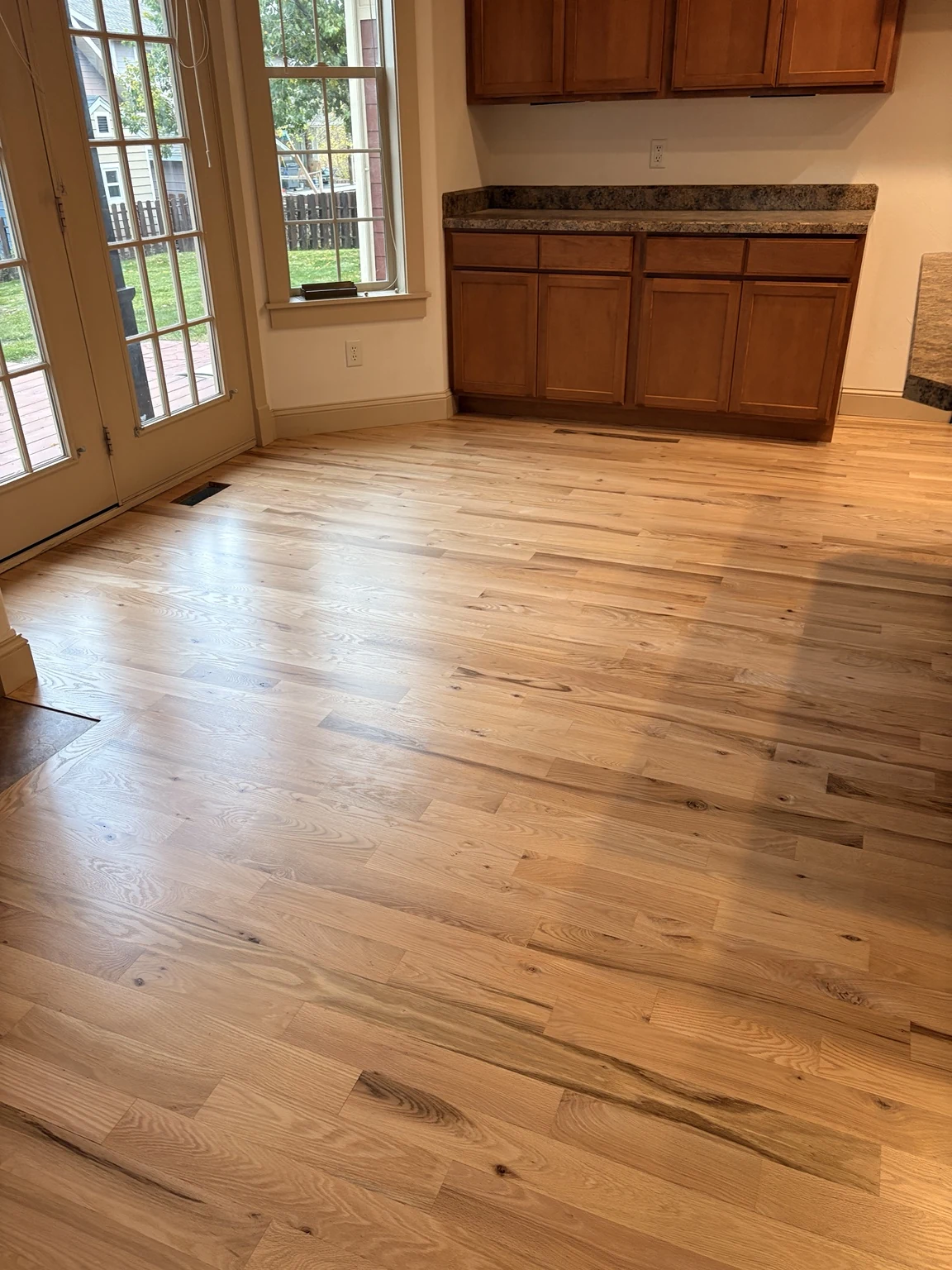 Natural hardwood flooring beside kitchen cabinets and patio doors